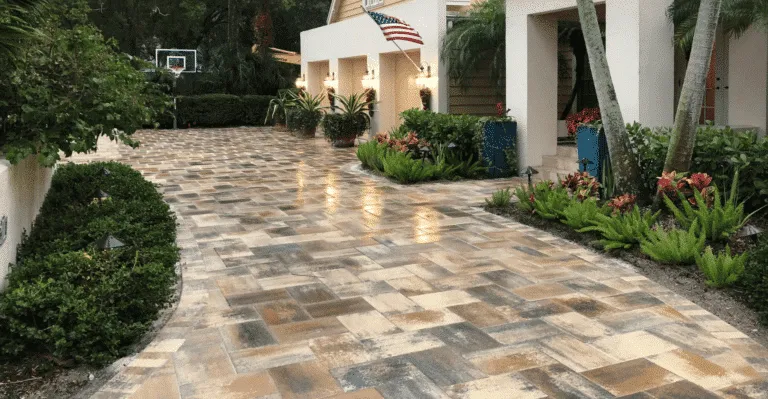 Long residential driveway paved with rectangular, multi-toned brown and tan interlocking pavers laid in a modified pattern.