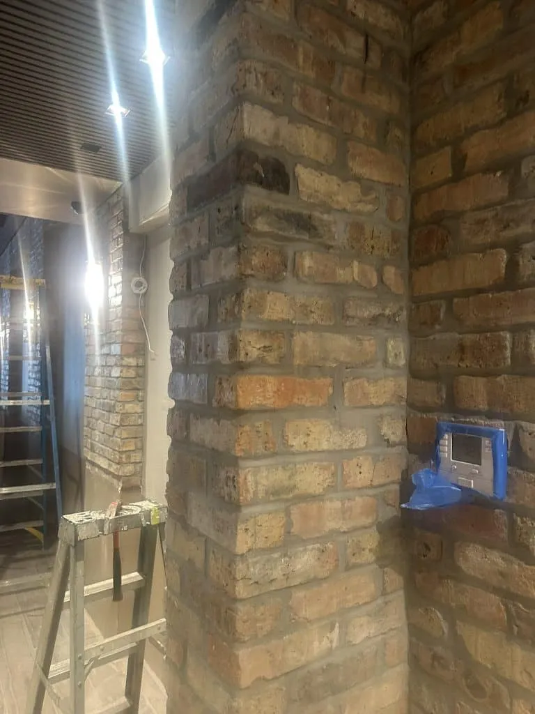Interior view of a column and walls finished with textured, multicolored exposed brickwork under construction lighting.