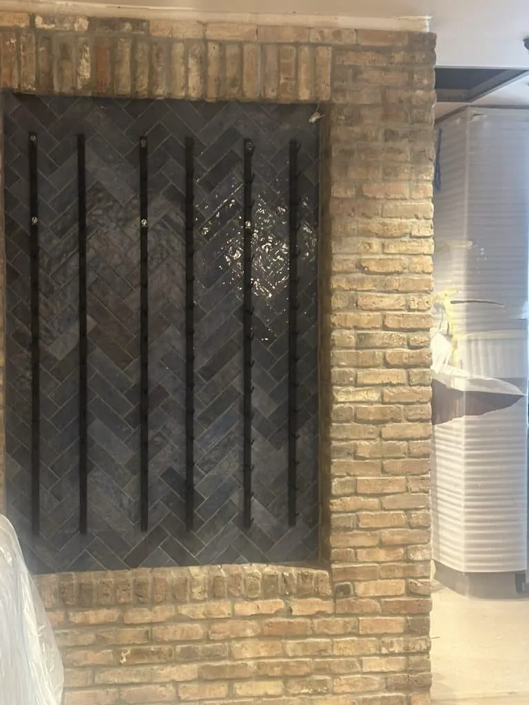 Interior feature wall framed in rustic brick with a central panel of glossy dark blue tiles set in a herringbone pattern.