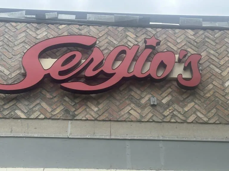 Exterior wall installation featuring a commercial sign (Sergio's) over a herringbone pattern brick wall. Specializing in decorative masonry, paver, and tile services near Miami, Florida.