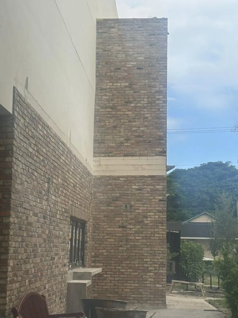 Corner of a building featuring brown brick cladding and a horizontal accent band of lighter stone or concrete.