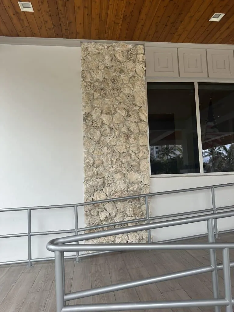 Commercial building exterior column clad in rough natural coral stone veneer next to a ramp with wood-look flooring.