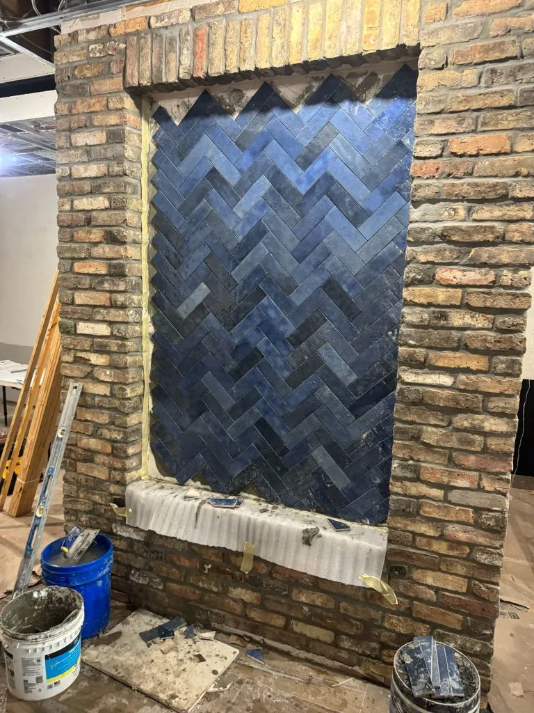Interior feature wall installation showing dark blue herringbone tiles framed by a rustic brick paver surround. Specialized paver and tile installation services in Miami, Florida.