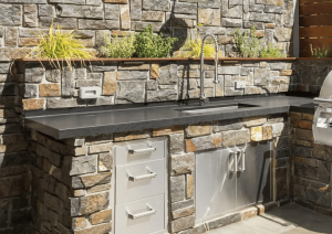 Elegant outdoor kitchen with natural stone walls constructed by Driveway & Paver Solutions in South Florida, blending durability with timeless beauty.